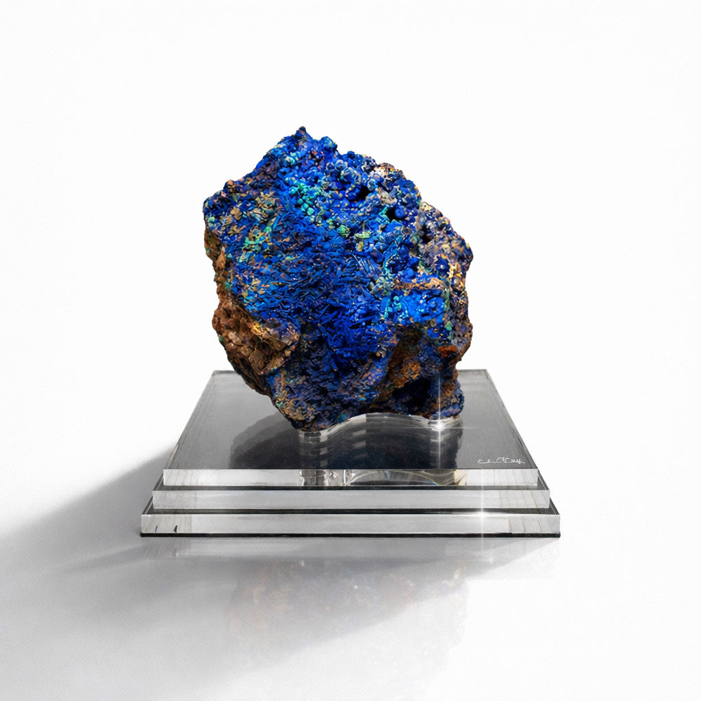 Blue mineral rock on a reflective silver platform against a white background