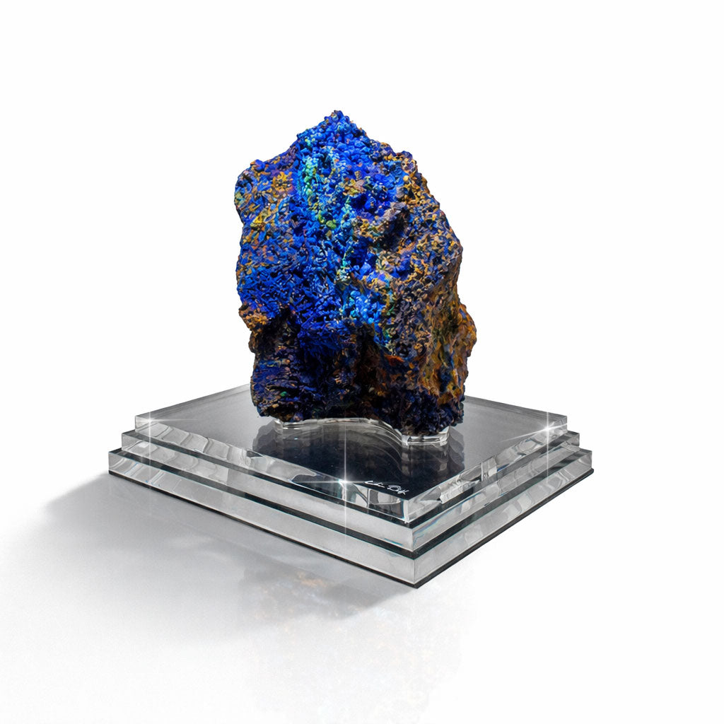 Blue and green mineral specimen on a clear glass stand against a white background